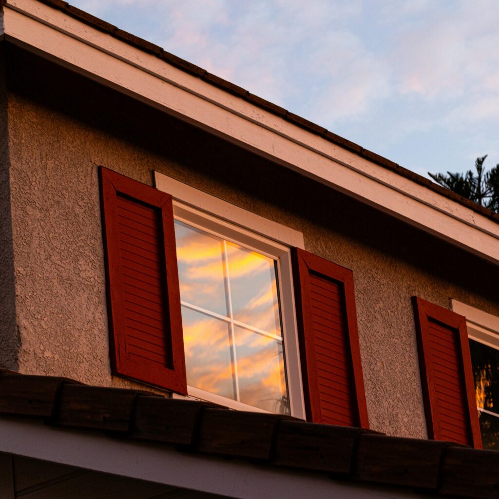 A vibrant sunset reflects on a window with red shutters, creating a warm ambiance.