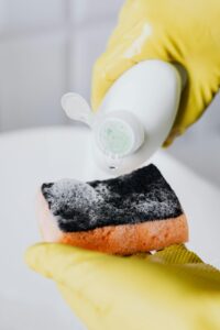 Person wearing gloves applies soap to a sponge for hygienic cleaning routine.
