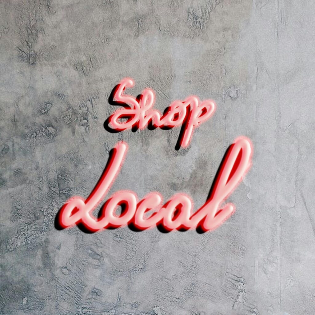 Bright neon "Shop Local" sign on a textured gray concrete wall, promoting local businesses.